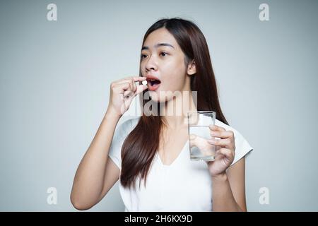 Schöne Frau, die die Kapsel der Arznei in der Hand hält und das mit Wasser gefüllte Glas hält Stockfoto