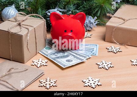 Ein Sparschwein, das auf Bargelden auf einem Tisch mit Geschenkschachteln, Schneeflocken und Tannenzweigen steht. Das Konzept von Erfolg und Wohlstand im Neuen Stockfoto