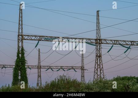 Metallkonstruktionen von Hochspannungsleitungen im hohen Gras. Im Hintergrund ist ein Sonnenuntergang Himmel. Das Konzept der Energiekrise in Asien und Stockfoto