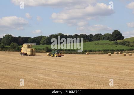 An einem Sommertag in der Nähe von Wakefield West Yorkshire in Großbritannien werden runde Heuballen von einem Traktor auf einen LKW gestapelt, um sie vom Feld zu transportieren Stockfoto