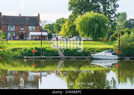 Blick auf den Fluss in Worcestershire, mit einem vertäuten Boot, Pub am Wasser, Weidenbaum und ruhigen Reflexen im Sommerlicht. Stockfoto