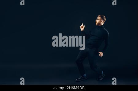In voller Länge von lustigen Hipster Kerl in schwarz Durchführung Show Tanz, der auf schwarzem Hintergrund isoliert. Stockfoto