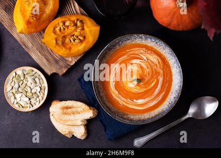 Vegetarisch pürierte gesunde Lebensmittel, Kürbiscremesuppe auf einem Teller auf dunklem Grund mit Gemüse. Stockfoto