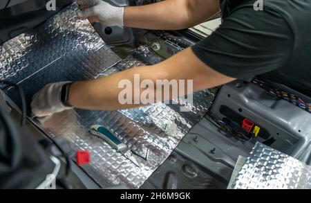 Arbeiter klebt Schalldämmmaterial auf die Innenseite des Fahrzeugbodens. Prozess der Installation der Schalldämmung im Auto. Stockfoto