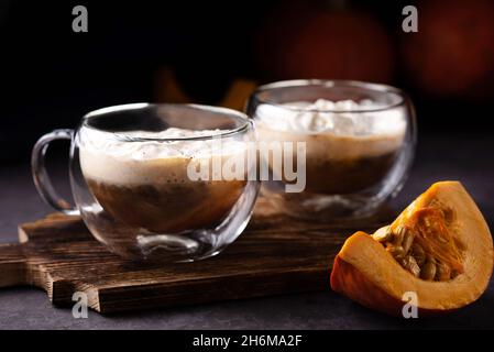 Zwei Tassen Kürbisgewürz Latte mit Schlagsahne auf dunklem Holzboden, herbstliche heiße Getränke. Stockfoto