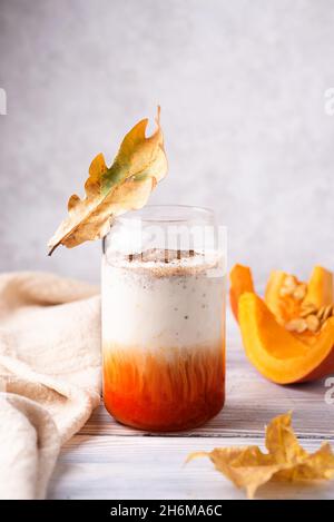 Kürbis gewürzter Latte im Glas auf weißem Holztisch, herbstlicher Kaffeedrink mit Schlagsahne. Stockfoto