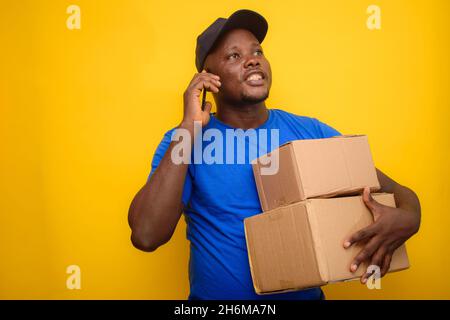 Afrikanischer Entsendungsmann, der in Nigeria mit einem Smartphone anruft, Boxen trägt und eine Mütze trägt Stockfoto