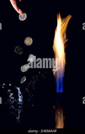 Ein Gasflackern verschlingt Geld. Gasgeld. Feuersäule und schwebender Euro-Münzen. Ein Spritzer Wasser fliegt herum. Stockfoto