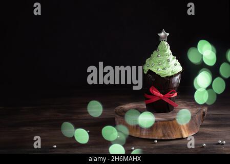 Muffin mit festlichem Dekor, Weihnachtskuchenform in Form eines Weihnachtsbaums mit Bokeh-Lichtern und Geschenken. Stockfoto