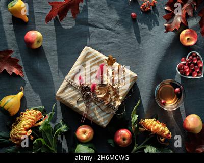 Orangefarbene Chrysanthemenblüten, trockenes Hasenschwanzgras, Kürbisse, Cranberry- und rote Eichenblätter. Herbstschmuck. Flacher Lay auf dunklem Textil. Stockfoto