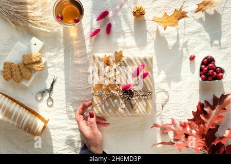 Herbstdekorationen - Preiselbeere, Kekse. Tee und trockene Eichenblätter. Flach liegend, Draufsicht auf unfarbigem Textil. Stockfoto