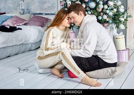 Liebevolles Paar sitzt in der Nähe von Weihnachtsbaum auf dem Boden. Stockfoto
