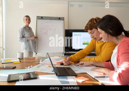 Eine Geschäftsfrau gibt eine Präsentation, während junge Kollegen über Graph sprechen Stockfoto