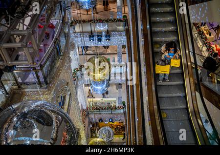 Eine Frau, die zu Weihnachten im Kaufhaus Selfridges in der Oxford Street, London, Großbritannien, auf der Rolltreppe einkauft, umgeben von riesigen Dekorationen. Selfridges Stockfoto