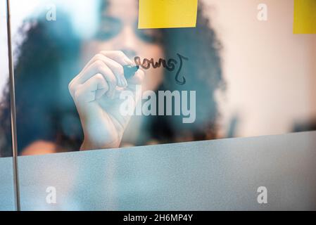 Geschäftsfrau, die Schrift an Glaswand im Büro Stockfoto