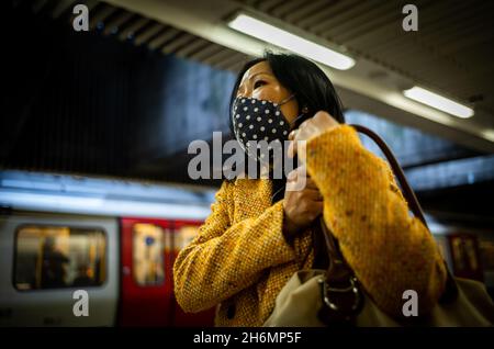 Eine asiatische Frau mit Gesichtsmaske wartet auf einen Zug in der Londoner U-Bahn. Aufgrund des Coronavirus Covid-19 waren Gesichtsmasken auf der Röhre obligatorisch Stockfoto