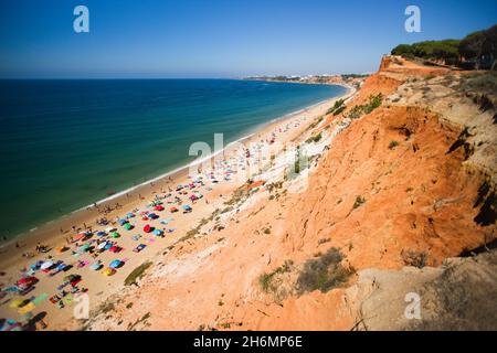 Orangefarbene Klippen, die im blauen Meer enden und Touristen die Sonne in 'Falesia' an der Algarve, Portugal, genießen Stockfoto