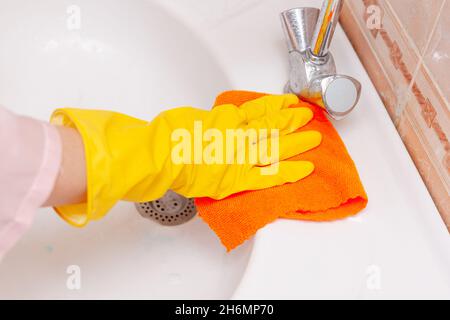 Die Hand in einem gelben Gummihandschuh wischt das Waschbecken im Badezimmer ab Stockfoto