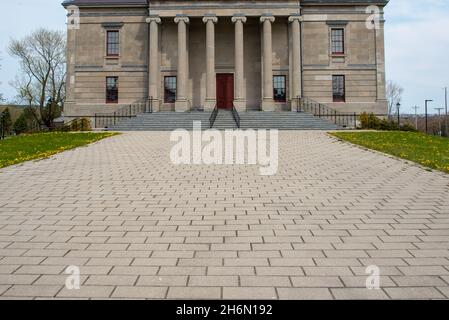 Ein breiter Ziegeleingang zu einem großen Regierungsgebäude. Es gibt eine rote Tür, eine graue Marmortreppe, hohe Fenster, runde Säulen und eine beigefarbene Außenwand. Stockfoto