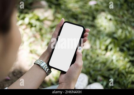 Draufsicht Mockup Bild einer Frau, die ein schwarzes Handy im Garten hält Stockfoto