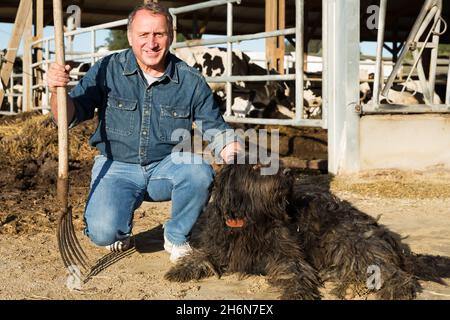 Bauer steht mit Hund auf dem Kuhhof Stockfoto