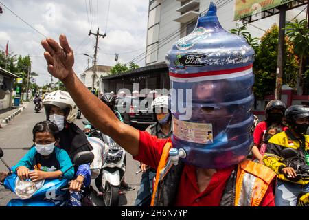 Yogyakarta, Sonderregion Yogyakarta, Indonesien. November 2021. Ali Akbar (52) Traffic Control Volunteer (Supeltas) nutzt eine Gallone Mineralwasser auf seinem Kopf, um sich vor dem COVID-19-Ausbruch zu schützen, während er den Verkehr in Yogyakarta, Indonesien, am Donnerstag, den 4. November 2021 kontrolliert. Indonesien hat mehr als 200 Millionen Impfziele für covid-19 und mehr als 63 % der indonesischen Bevölkerung haben den Impfstoff covid-19 erhalten. Die indonesische Regierung hofft, dass sich die indonesische Wirtschaft mit diesem Impfstoff bald erholen wird. (Bild: © Slamet Riyadi/ZUMA Press Wire) Stockfoto