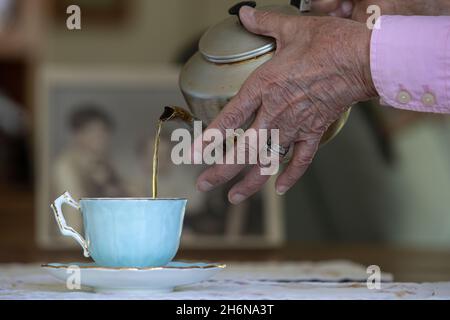 Generisches Foto einer Frau mit alten Händen, die eine Tasse Tee aus einem Topf in eine porzellbecher gießt. Stockfoto