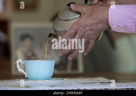 Generisches Foto einer Frau mit alten Händen, die eine Tasse Tee aus einem Topf in eine porzellbecher gießt. Stockfoto