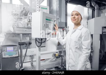 Fabrikingenieurin Frau, die das Bedienfeld der Maschine in der Mühle Mehl, in der Produktionsanlage für Milchprodukte betreibt. Stockfoto