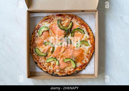 Pizza mit Lachs Gravlax und Avocado-Scheiben in Pizza Box. Bereit zum Essen. Stockfoto