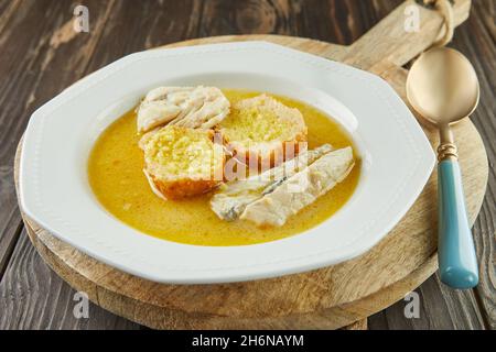 Weiße Fischsuppe - mit Baguette bestattet, in weißer Platte auf Holzbrett. Französische Gourmetküche. Stockfoto