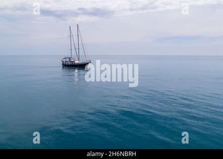 Eine Yacht segelt am Meer entlang, vor der Kulisse eines azurblauen Himmels. Stockfoto