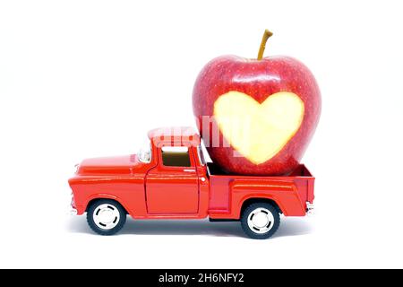 Roter Spielzeug Pickup-Truck mit einem Apfel mit Herzform eingeschnitzt geladen, isoliert auf weißem Hintergrund. Stockfoto