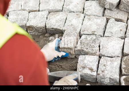 Arbeiter machte Gehweg aus Ziegelsteinen mit Hammer in der Hand, über die Schulter-Ansicht. Wartungsarbeiten am Pflaster mit ineinander verschränktem Pflasterstein Stockfoto