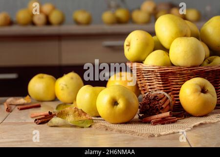 Frische saftige Äpfel im Korb und Zimtstangen auf einem Küchentisch. Stockfoto