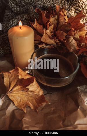 Brennende Kerze und eine große Tasse heißen schwarzen Kaffee in einem gemütlichen herbstlichen Stillleben mit trockenen Blättern. Stockfoto