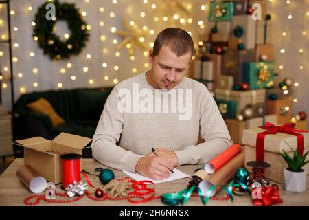 Glücklicher Mann, der am Tisch sitzt und etwas auf Papier schreibt Stockfoto