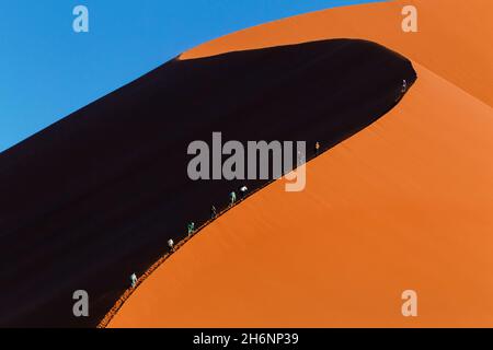 Touristen und Reisende erklimmen die höchste Düne 45 bei Sonnenuntergang. Sossusvlei, Dune 45, Namib Naukluft, Namibia Stockfoto