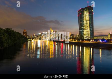 Die beleuchtete Europäische Zentralbank, die EZB und die farbenfrohe Skyline von Frankfurt spiegeln sich in der späten Abenddämmerung vom Arthur-von-Vineyard-Steg im Main wider Stockfoto