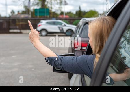 Frau fährt ihr Auto sehr aggressiv und gibt mit seinem Handfinger, virw von hinten, eine Geste Stockfoto