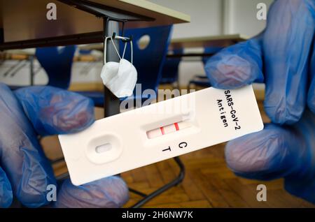 FOTOMONTAGE, positiver Antigen-Schnelltest, Gesichtsmaske hängt am Studierendentisch, Präsenzunterricht, Corona-Krise, Stuttgart, Baden-Württemberg Stockfoto