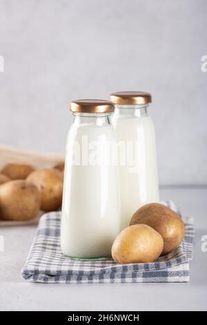 Vegane Milch auf pflanzlicher Basis in zwei Flaschen. Alternative Kartoffelmilch und Kartoffelknollen auf grauem Tisch - Bild Stockfoto