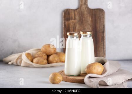 Vegane Milch auf pflanzlicher Basis in zwei Flaschen. Alternative Kartoffelmilch und Kartoffelknollen auf grauem Tisch - Bild Stockfoto