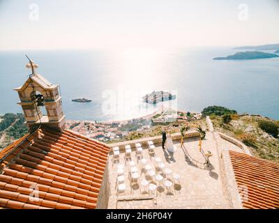 Braut und Bräutigam stehen auf der Aussichtsplattform vor der Kirche Sveti Sava mit Blick auf die Insel Sveti Stefan. Montenegro. Blick von oben Stockfoto