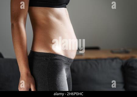 Junge Frau Seitenansicht des Körpers. Geschwollener Bauch. Schwangerschaft. Diastasis recti nach der Geburt des Kindes. Fitness-Übungen und Ernährung zur Gewichtsabnahme. Stockfoto