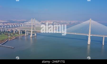 Luftaufnahme der schönsten portugiesischen Brücke in Lissabon, Vasco da Gama. Morgen neblige Meereslandschaft. Blick auf die Stadt, mit Hochhäusern. Stockfoto