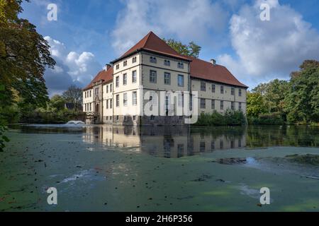 Wasserschloss Strünkede in Herne, Deutschland. Blick auf das Herrenhaus mit Wasser im Vordergrund und teilweise bewölkten Himmel zu Beginn des Herbstes. Stockfoto