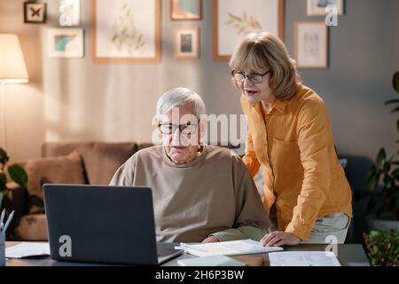 Ältere Paare, die zusammen am Tisch einen Laptop benutzen, lernen, Online-Dienste zu Hause zu nutzen Stockfoto