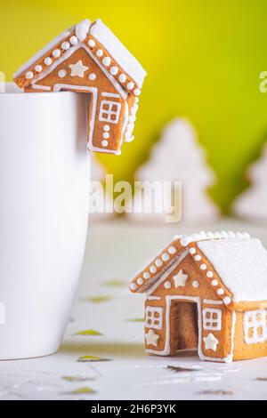 Lebkuchenhütten und eine Tasse Milch auf einer weißen Betonoberfläche mit Funkeln, Nahaufnahme. Weihnachtsfeier Konzept Stockfoto