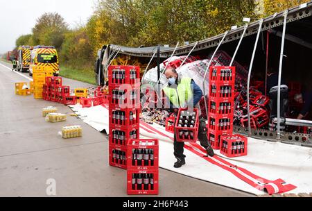 Talkau, Deutschland. November 2021. Am Unfallort auf der Autobahn A24 stapelt ein Mann Getränkekisten von der Rückseite eines umgedrehten Lastwagens. Der Lastwagen hatte die Fahrbahn am Morgen verlassen und umgestrostet, wobei die Last auf der Fahrbahn verteilt wurde. (To dpa 'Truck loaded with crates of drinks overturns on motorway') Quelle: Daniel Bockwoldt/dpa/Alamy Live News Stockfoto